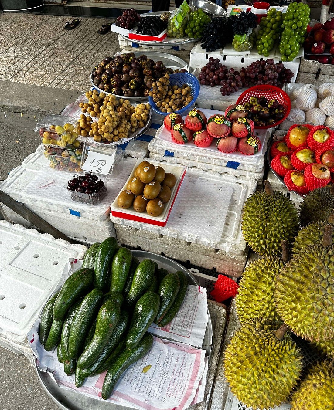 Fresh tropical fruits at a bustling Vietnamese market, featuring durian, avocado, and mangosteen.