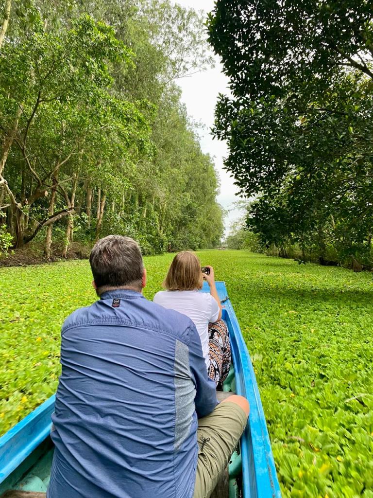 Tourists cruise through Lung Ngoc Hoang Nature Reserve, passing lush wetlands and narrow canals in the peaceful Mekong Delta.