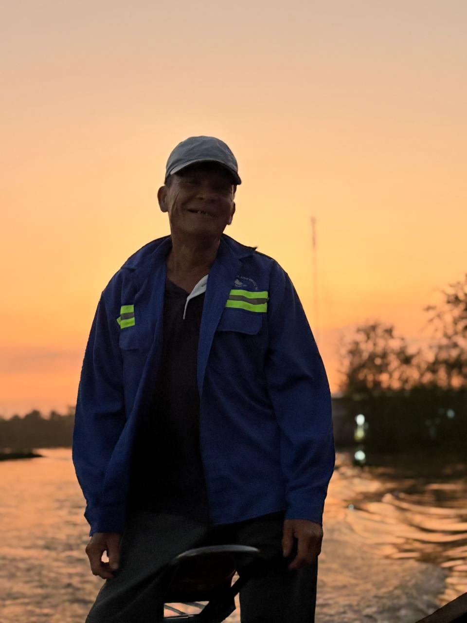 Smiling local boat driver navigating the Mekong Delta at sunrise in Can Tho, Vietnam, offering an authentic floating market experience.