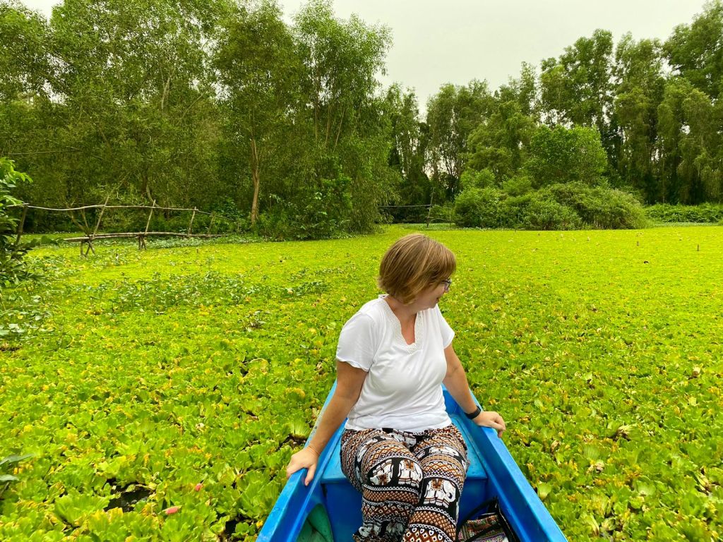 A woman sitting in a boat, gliding through the green wetlands of Lung Ngoc Hoang Nature Reserve.