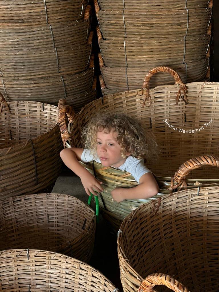 A young child sitting inside large handcrafted bamboo baskets at Lung Ngoc Hoang Nature Reserve, Vietnam.